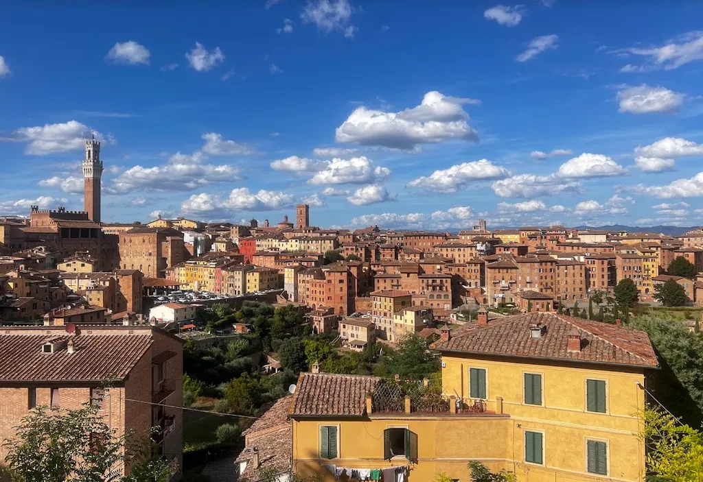 Vue panoramique de la ville de Sienne, en Italie, avec ses toits en terre cuite et le ciel bleu parsemé de nuages blancs.